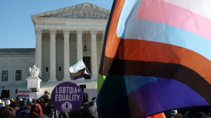 people with signs and flags supporting LGBTQ rights rally outside of the Supreme court