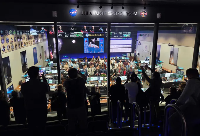 Silhouetted people look through a glass window and take pictures of NASA's mission control room in Houston in the hours before Artemis II swings around the moon.