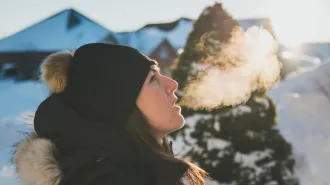 A woman wearing a wool hat exhales a visible breath in the cold