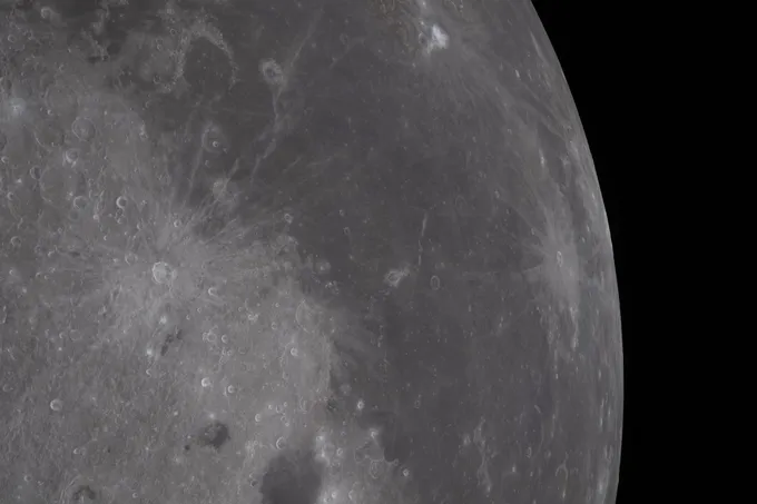 Flat gray moon terrain is punctuated by bright craters surrounded by rays