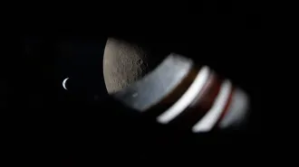A view through the spacecraft window, wiht some of the window itself visible. The moon fills the right side of the frame and the smaller Earth is to the left.