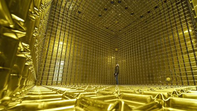 A person stands inside a large, gold, cube-shaped particle detector