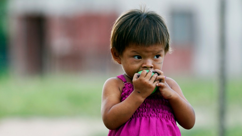 A young child holds food to their mouth outdoors.