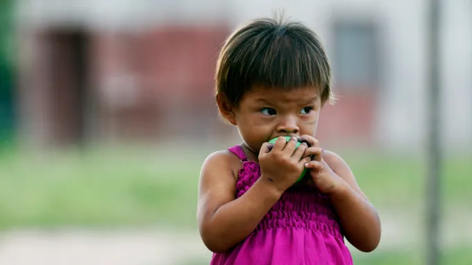 A young child holds food to their mouth outdoors.