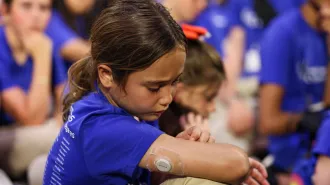 A girl in a purple T-shirt sits in a crowd of other kids also wearing purple. A device, called a continuous glucose monitor, is visible on the back of her arm.