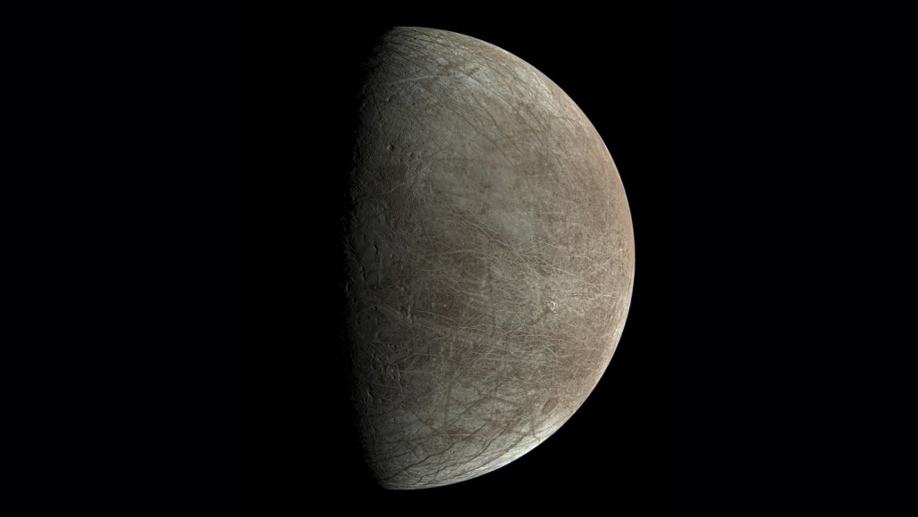 A brownish-gray moon crisscrossed with lines with the left half in shadow.