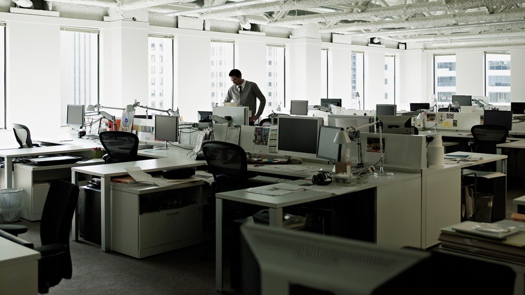 A man stands among a sea of empty desks in an office.