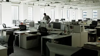 A man stands among a sea of empty desks in an office.