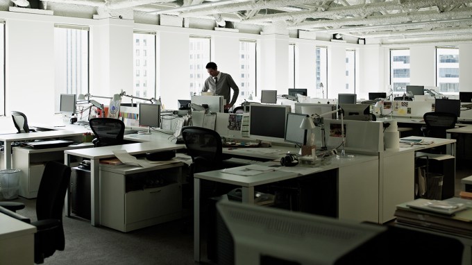 A man stands among a sea of empty desks in an office.