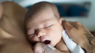 a newborn baby, with eyes closed and mouth open, rests on their parent's chest