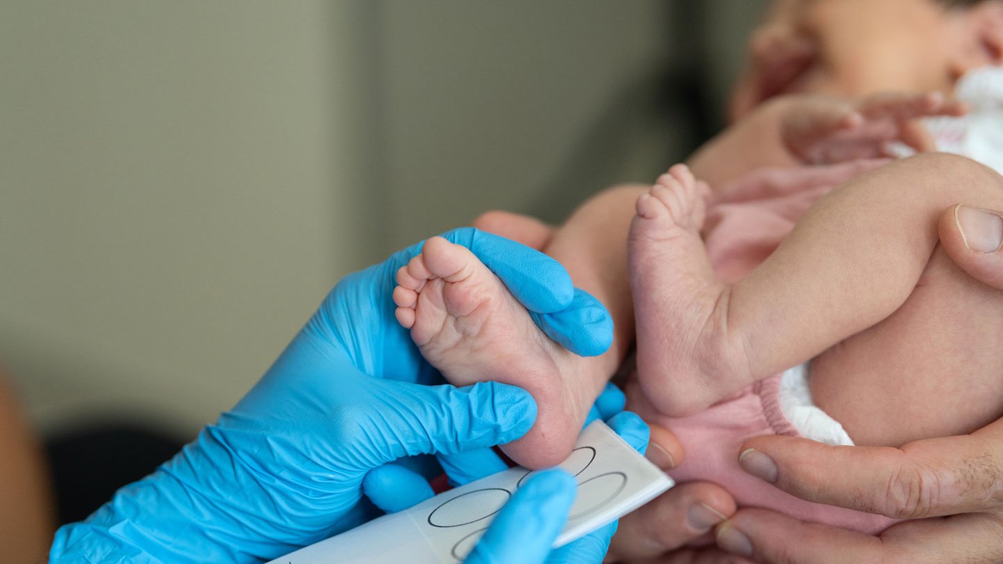 A health care provider wearing blue gloves presses a newborn baby's heel to a card.