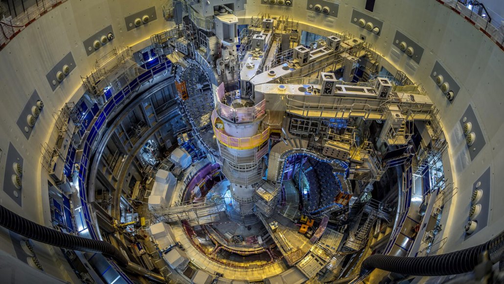 Interior view of the ITER fusion reactor under construction, showing a massive doughnut-shaped chamber lined with components and scaffolding.