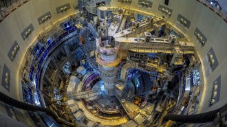 Interior view of the ITER fusion reactor under construction, showing a massive doughnut-shaped chamber lined with components and scaffolding.