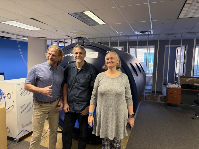 Joseph Dituri, Clinton Hughes and Judith Klein-Seetharaman stand in front of a large cylindrical chamber, built for ASU's XPRIZE Healthspan bid