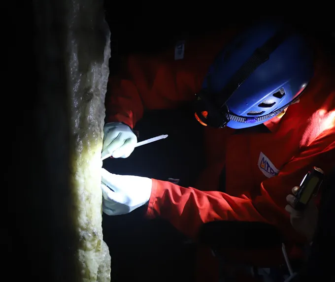 A photo of a researcher with a headlamp sampling a stalagmite in a cave.