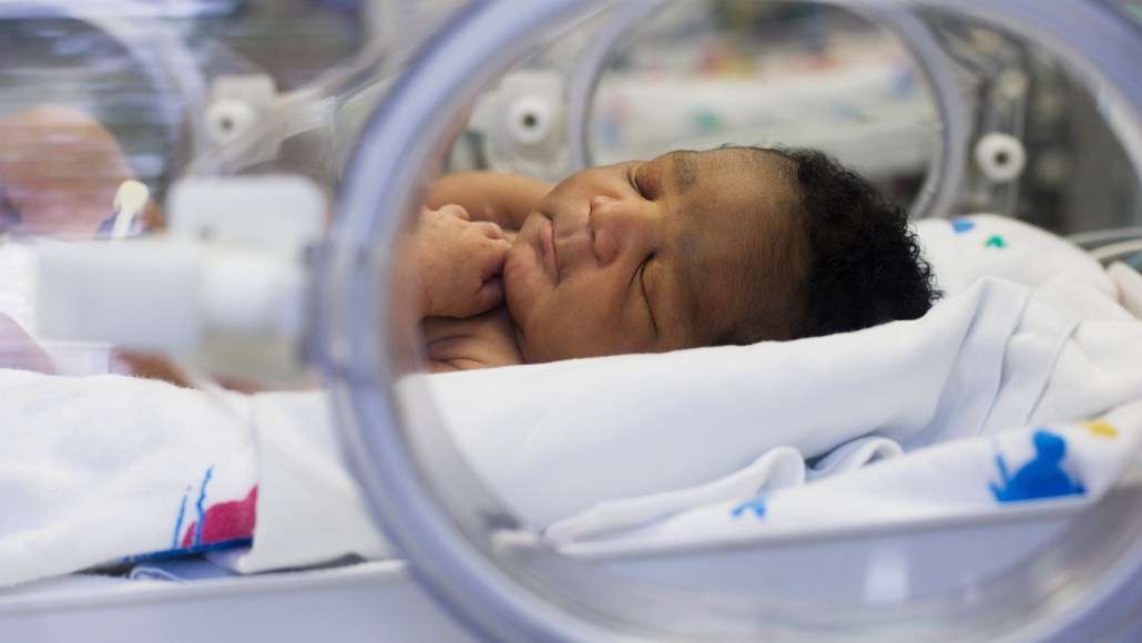A peacefully sleeping baby lies on a NICU bed with protective clear barriers