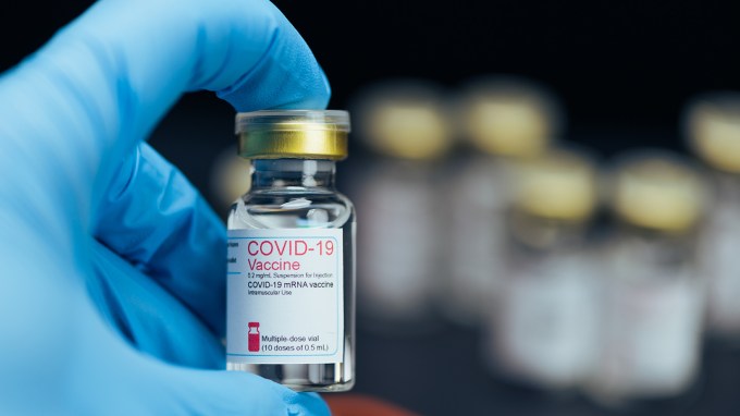 A blue gloved hand holds a COVID-19 vaccine bottle.