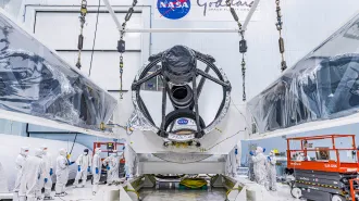 The large Nancy Roman Space Telescope sits in a hangar, surrounded by workers in protective suits.