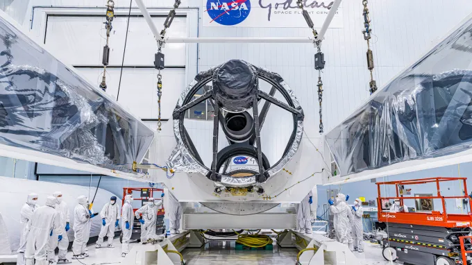 The large Nancy Roman Space Telescope sits in a hangar, surrounded by workers in protective suits.