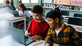 Two students sitting at a desk looking at a laptop screen.