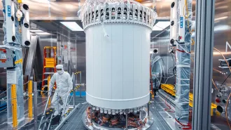 A person stands next to a large cylindrical piece of the LZ detector