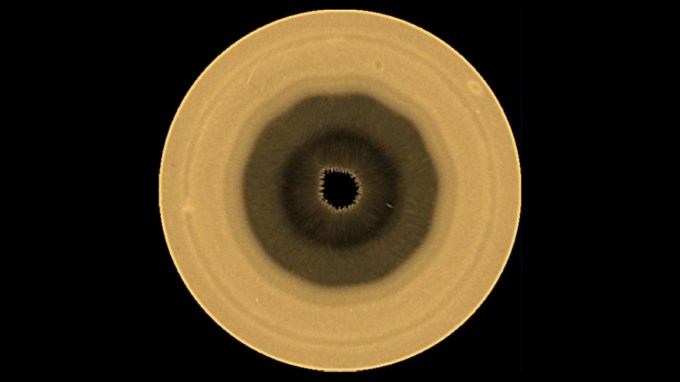 A golden colored orb has a very dark center, surrounded by lightening colors as you move outward. It shows a weird weather pattern at Saturn's south pole.