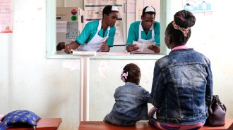A mother and daughter in denim jackets sit on a bench with their backs to the camera, facing an open window where two uniformed nurses look at paperwork