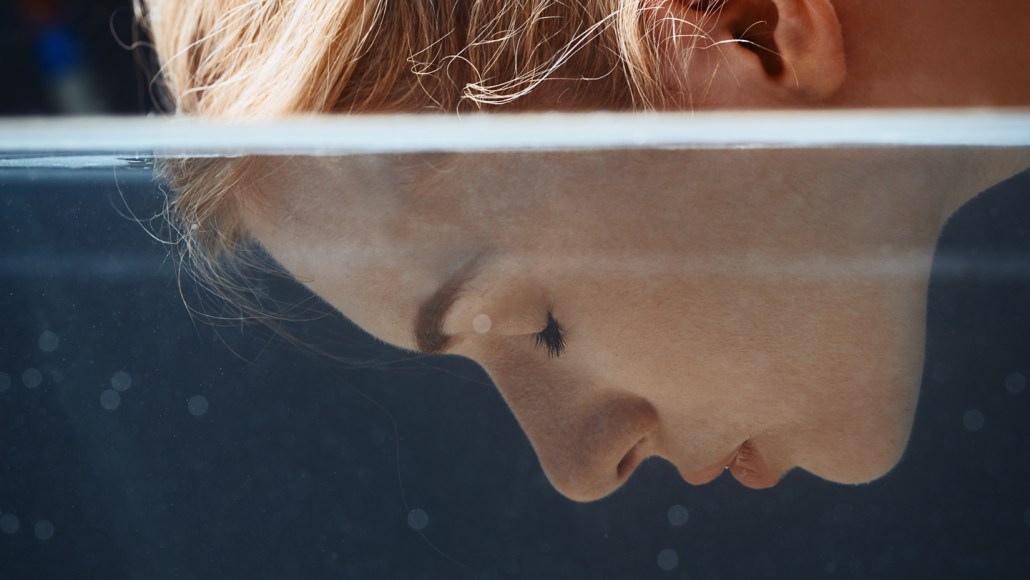 Close-up of a woman with her face partly submerged in water, her eyes closed beneath the surface.