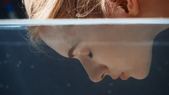 Close-up of a woman with her face partly submerged in water, her eyes closed beneath the surface.